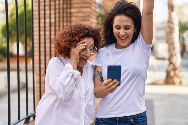 Duas mulheres mãe e filha juntas usando smartphone na rua