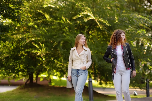 Duas mulheres novas bonitas que falam ao andar em Sunny Park. Comunicação e fofoca.