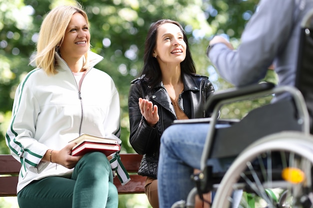 Duas mulheres se comunicam com um homem em uma cadeira de rodas em um parque de amizade com pessoas com