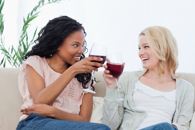 Duas mulheres segurando copos de vinho estão sorrindo umas para as outras