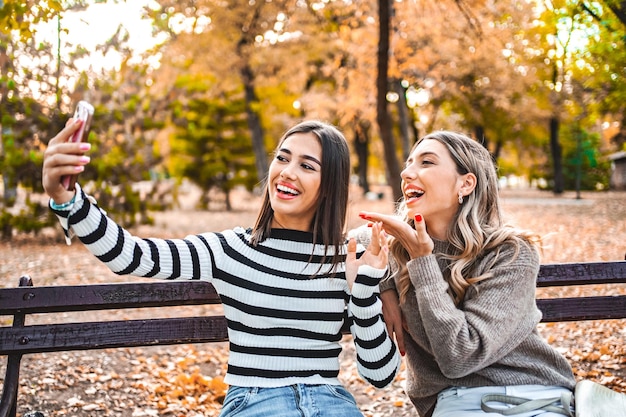 Duas mulheres sentadas em um banco do parque tirando uma selfie