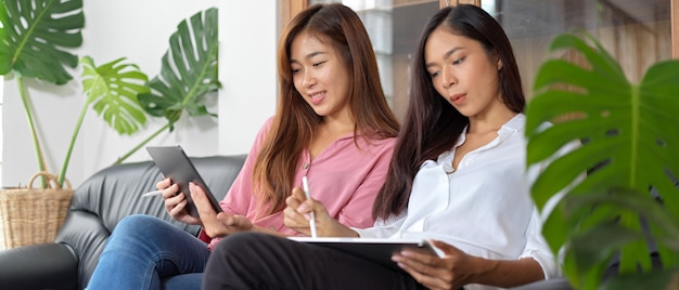 Duas mulheres sentadas no sofá, usando smartphone e tablet