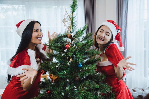 Duas mulheres sexy Santa decorando as árvores de Natal da festa de Natal com feliz em casa.
