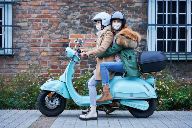 Foto duas mulheres usando máscaras e se deslocando de scooter