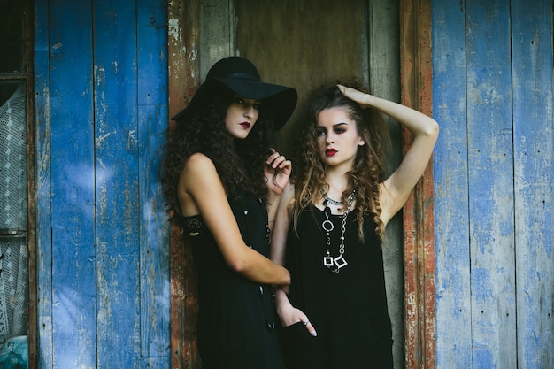 Duas mulheres vintage como bruxas, posando ao lado de um prédio abandonado na véspera do Halloween