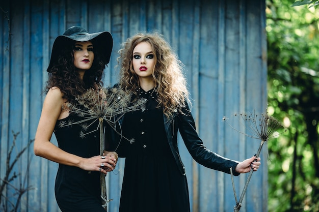 Duas mulheres vintage como bruxas, posando em frente a uma casa abandonada na véspera do Halloween