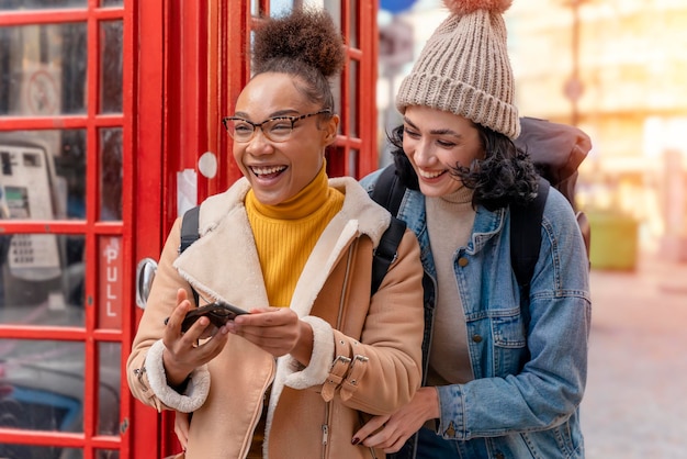 Duas namoradas amigas e mulheres tirando selfie contra uma cabine telefônica vermelha na cidade da Inglaterra