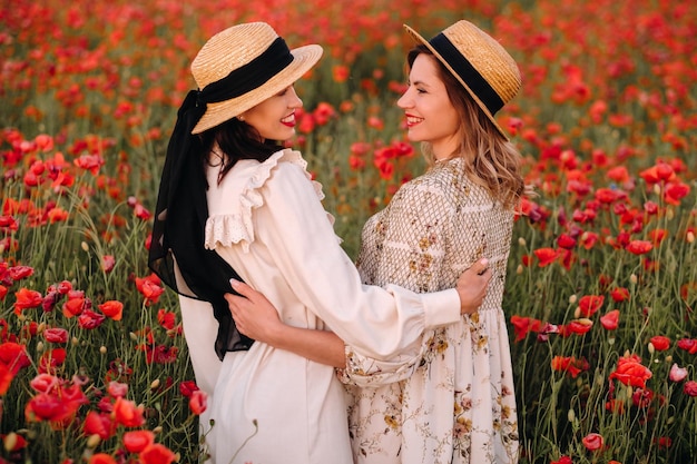 Duas namoradas em vestidos e um chapéu em um campo de papoulas no verão ao pôr do sol