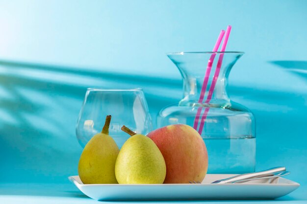 Duas peras e uma maçã em uma bandeja atrás de uma garrafa e um copo de água perfeito café da manhã saudável