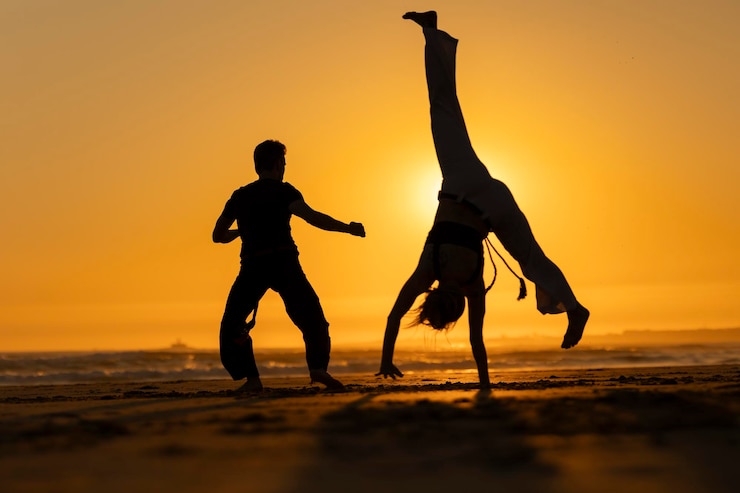 Foto duas pessoas a praticar capoeira na praia ao pôr-do-sol
