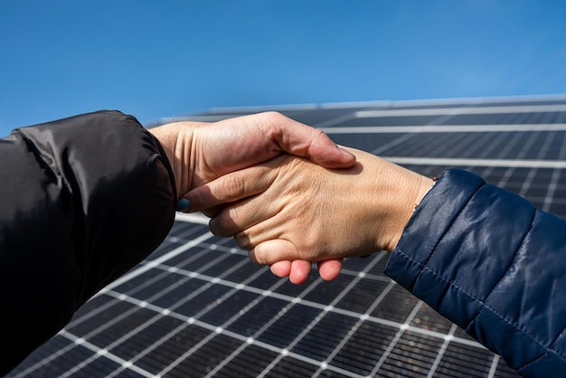 Duas pessoas apertando as mãos contra um painel solar depois de assinar um acordo de energia renovável