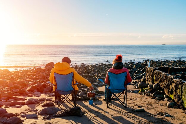 Foto duas pessoas em cadeiras de praia juntas na praia de inverno céu azul ensolarado horizonte inverno frio britânico