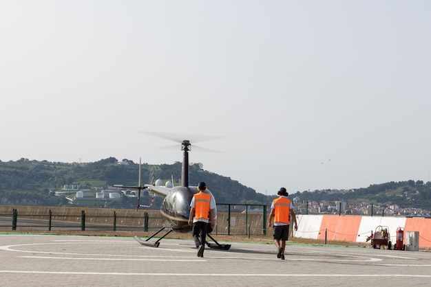 Duas pessoas em coletes refletivos caminham até o helicóptero