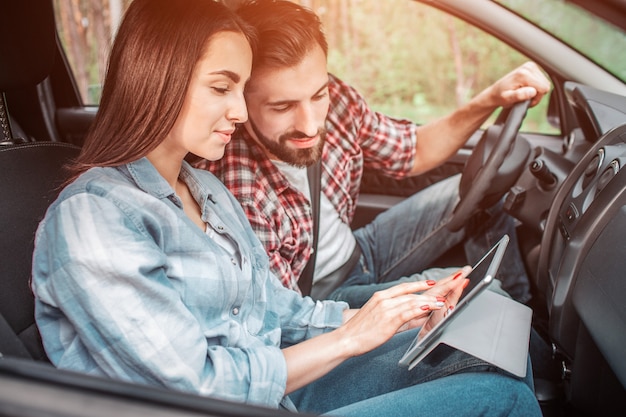 Duas pessoas estão sentadas juntas no carro e olhando no tablet que a  garota está segurando. eles estão olhando para a tela com interesse e  emoção.