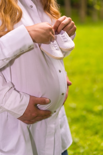 Duas pessoas irreconhecíveis com duas botinhas de bebê na barriga de uma mulher grávida em uma floresta