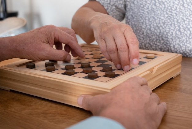 Foto duas pessoas sênior em casa enquanto jogava um jogo de damas na mesa de madeira.