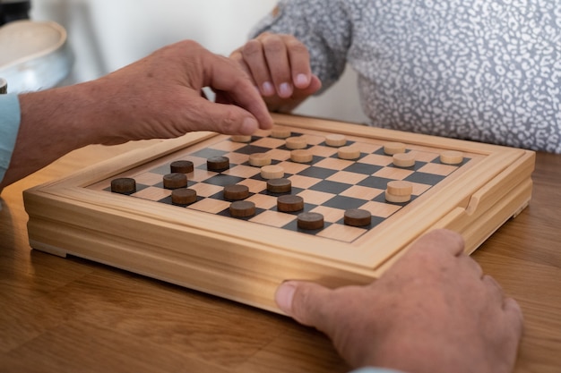 Foto duas pessoas sênior em casa enquanto jogava um jogo de damas na mesa de madeira.