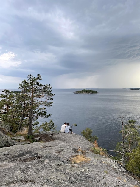 Duas pessoas sentadas em uma pedra com vista para o lago