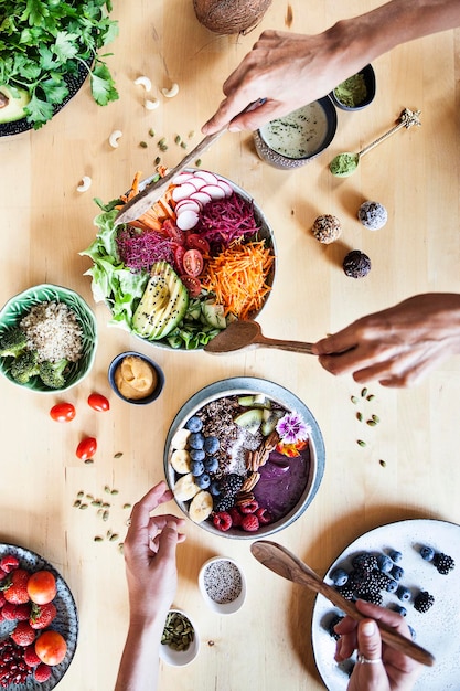 Duas pessoas servindo buda bowl na mesa de madeira com legumes frescos crus e saudáveis