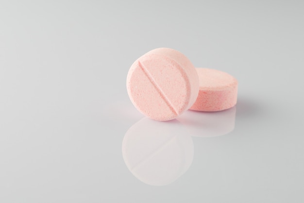 Duas pílulas ascórbicas médicas rosa sobre um fundo claro com reflexão. Isolado
