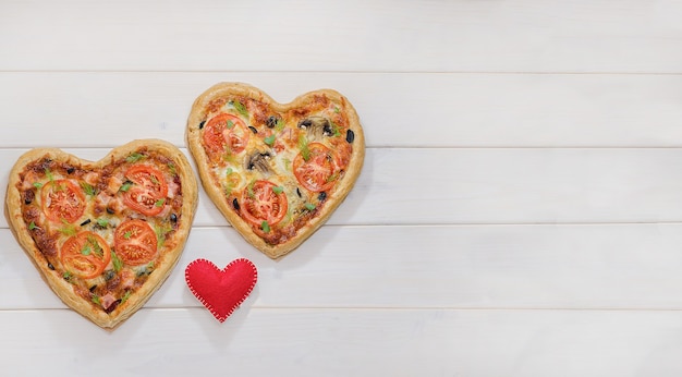 Duas pizzas em forma de coração em uma mesa de madeira branca com espaço de cópia com um coração vermelho. dia dos namorados, amor.