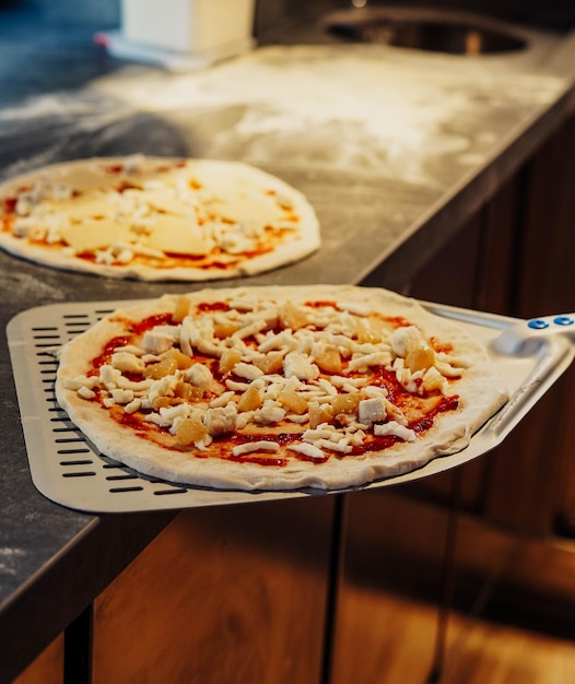 Duas pizzas em uma pá com uma sendo cozida.