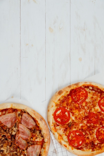 Duas pizzas fatiadas caseiras na vista superior da mesa de madeira branca