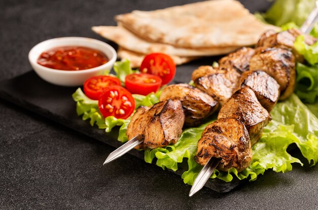 Duas porções de shish kebab num prato de pedra com salada.