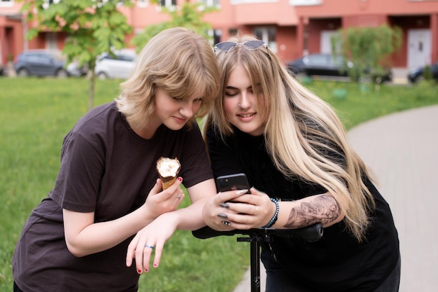 Duas raparigas engraçadas estão sentadas num baloiço na cidade e a tirar selfies com o telemóvel.