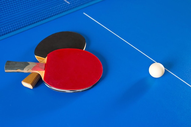 Duas raquetes para tênis de mesa e uma bola branca na mesa azul Um jogo de pingue-pongue Jogos de esporte
