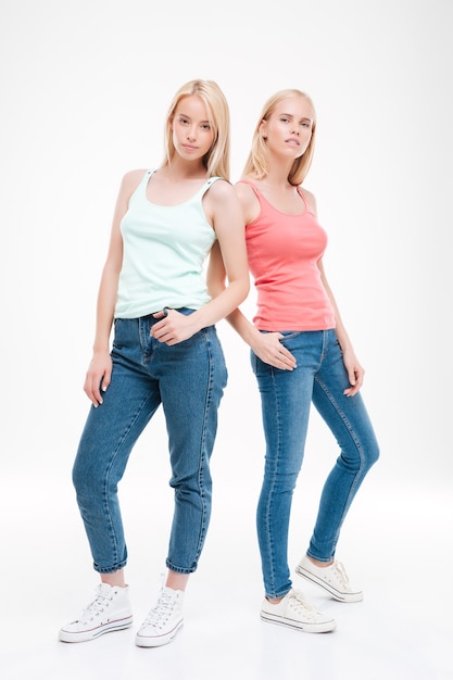 Duas senhoras vestidas com camisetas e jeans posando. Isolado sobre a parede branca. Olhando para a frente