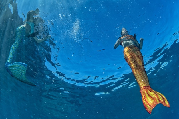 Duas sereias nadando debaixo d'água no mar azul profundo