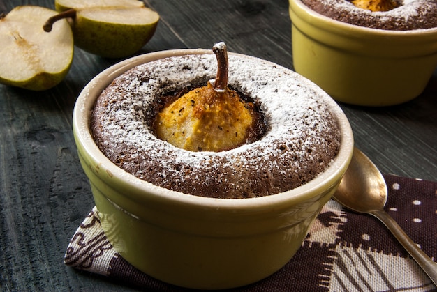 Duas sobremesas de chocolate com uma pêra em uma mesa de pedra preta, vista superior