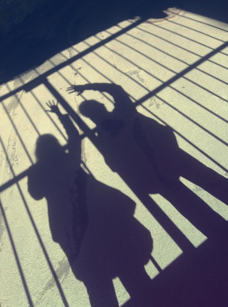 Foto duas sombras a sombra de um homem e a sombra de uma mulher acenam uma mão de saudação contra o fundo da treliça
