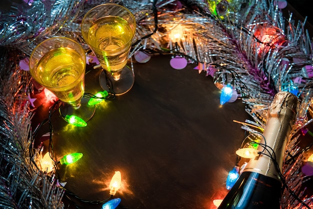 Duas taças com champanhe e garrafa sobre uma mesa de madeira decorada com acessórios de Natal para celebrar o ano novo e o Natal. Noite Romantica. O brilho das guirlandas. Dia dos Namorados