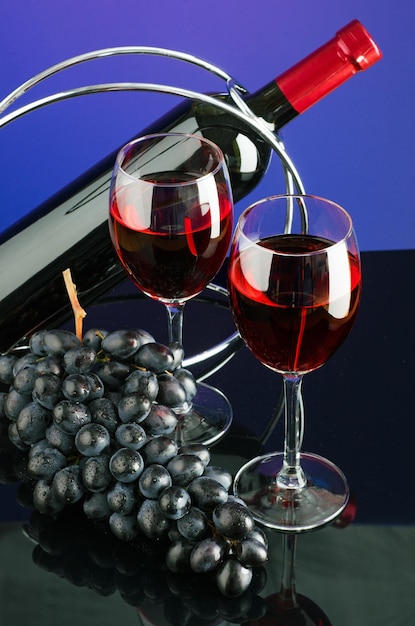 Duas taças com vinho tinto, garrafa e escova de uvas azuis sobre fundo de cor brilhante
