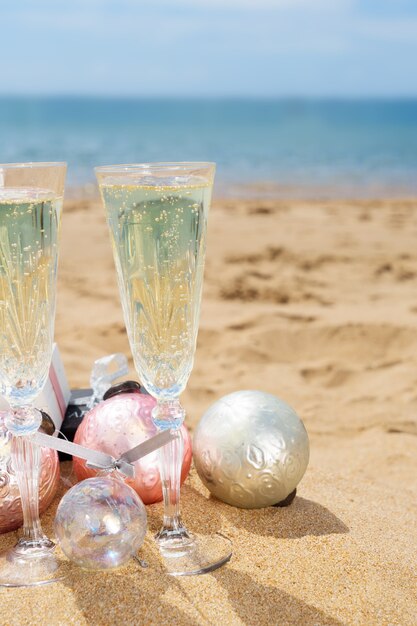 Foto duas taças de champanhe de natal com presentes de natal e decorações na praia à beira-mar