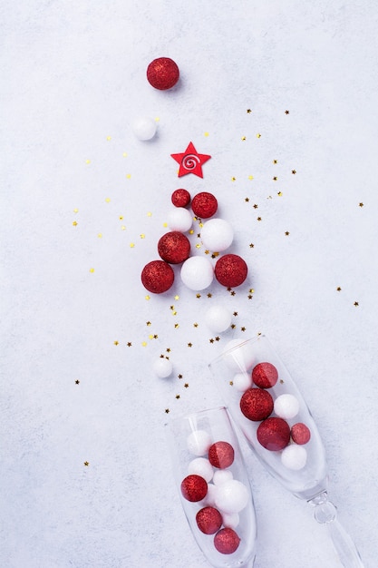 Duas taças de champanhe e garrafa de champanhe de Natal com granulado em forma de árvore de Natal feita de bolas de brinquedos vermelhas e brancas decoradas confetes dourados em branco.