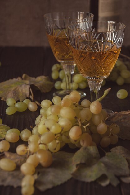 Duas taças de cristal com vinho branco, uvas e folhas secas