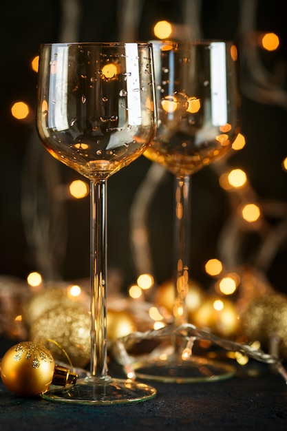 Duas taças de vinho e bolas douradas de Natal contra luzes douradas desfocadas