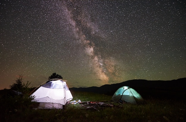 Duas tendas de turista iluminadas à noite sob o céu estrelado lindo incrível com a Via Láctea.