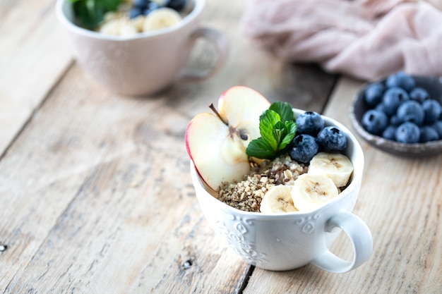 Duas tigelas de aveia ou granola com mirtilos, maçã, mel e hortelã em um fundo de madeira rústico. Copie o espaço