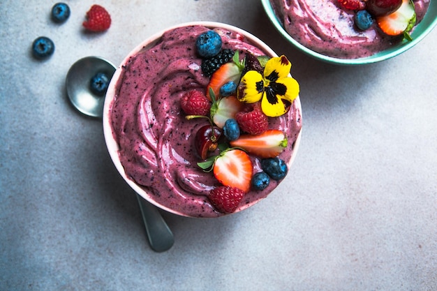 Duas tigelas de smoothie de açaí de verão com mirtilos de morangos em fundo de concreto cinza Tigela de café da manhã com frutas e cereais closeup vista superior comida saudável