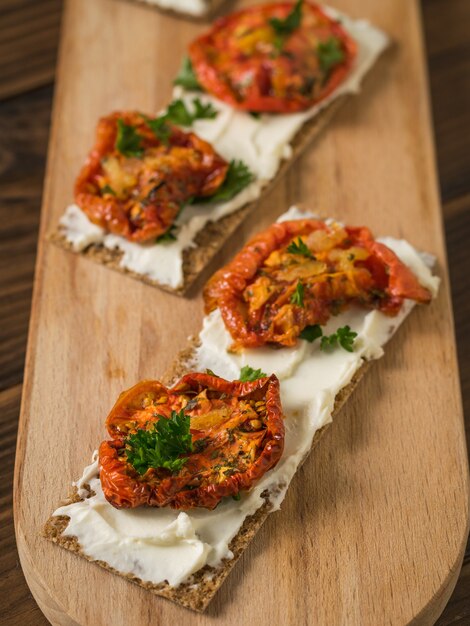 Duas torradas de pão em uma tábua de cortar com cream cheese e tomates secos ao sol em uma mesa de madeira. lanche vegetariano de queijo cottage e tomate.