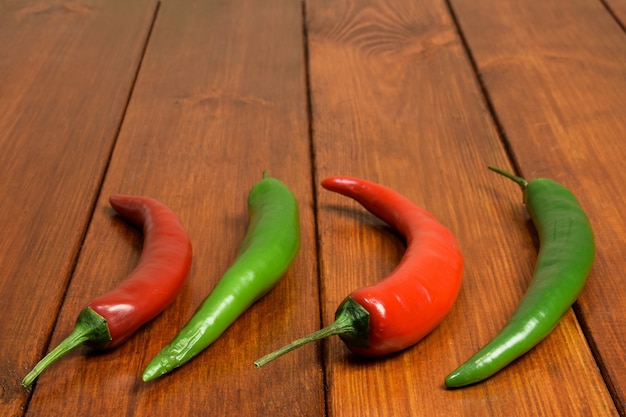 Duas vagens vermelhas e duas verdes de pimenta fresca sobre uma mesa de madeira marrom em primeiro plano