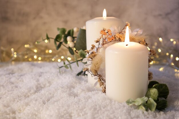 Duas velas brancas decoradas na decoração de Natal na neve contra o fundo das luzes