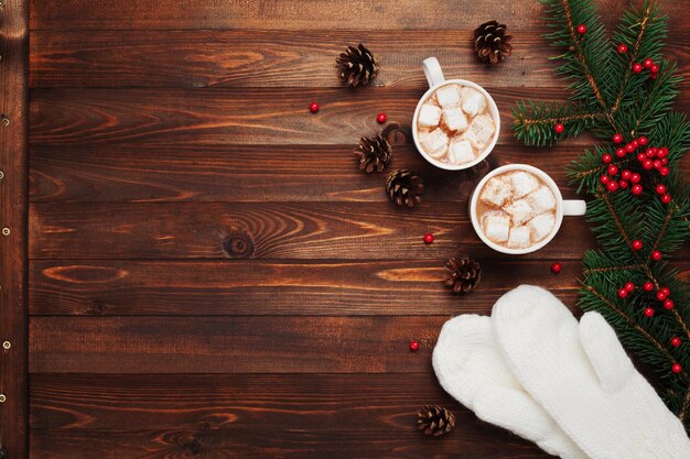 Duas xícaras de cacau quente ou chocolate com luvas de marshmallow, decoração de natal e abeto em madeira