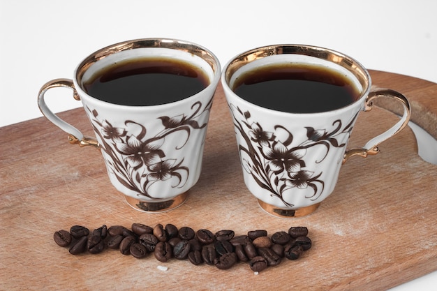 Duas xícaras de café brancas com grãos de café em uma placa arborizada.