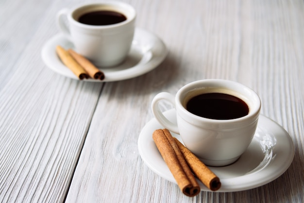 Duas xícaras de café com canela em uma mesa de madeira branca