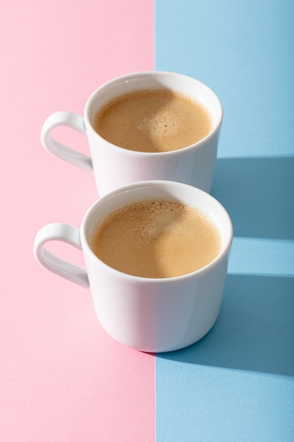 Duas xícaras de café em um fundo rosa pastel e azul, fotografia com sombras contrastantes